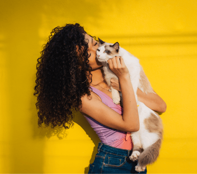 a woman holding a cat that is sitting on a yellow wall