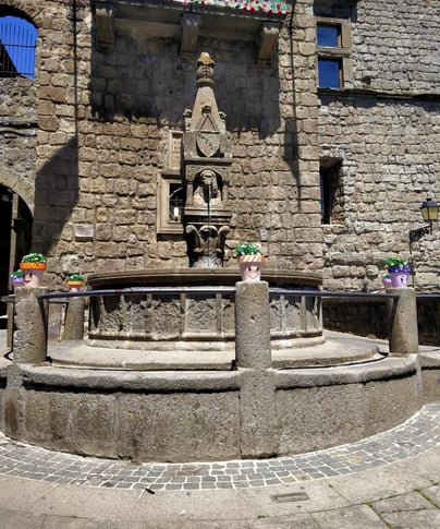 a fountain with a clock on it in front of a stone building