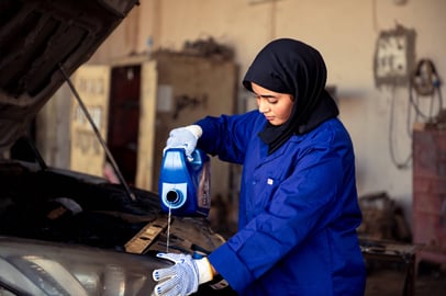 Sudanese woman mechanic pouring engine oil into a car.