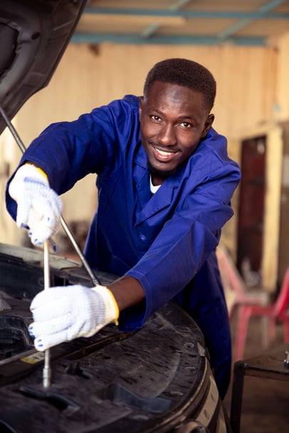 Sudanese mechanic smiling while fixing a car engine, TVET 
