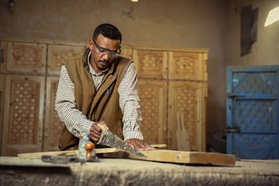 Sudanese carpenter cutting wood with a handsaw in a workshop.