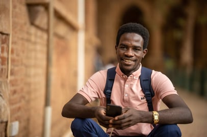 Smiling Sudanese student with phone and backpack