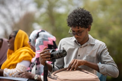 Young Sudanese man preparing his camera during an outdoor workshop.