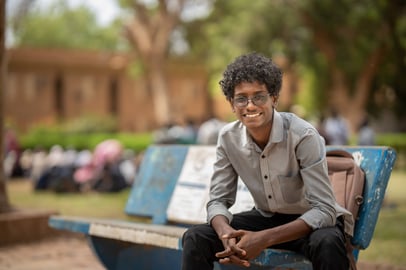 Sudanese student sitting on a bench and smiling on university of khartoum campus.