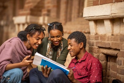 Close-up of three smiling Sudanese students discussing notes together.