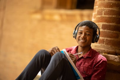 Sudanese student smiling while studying and wearing headphones outdoors.