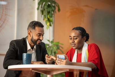 Sudanese man and woman discussing something on a phone at a coffee table.