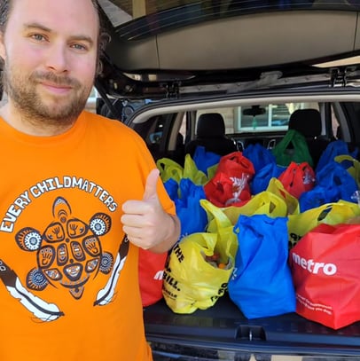 A smiling founding member beside a van trunk filled with donated food items