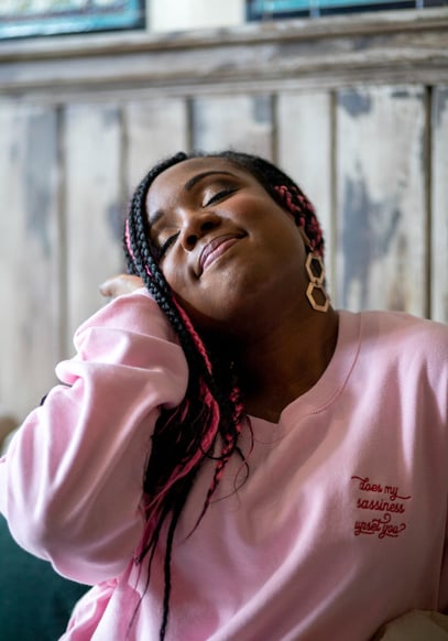 A Black woman with long pink and black hair and a pink jumper with red writing