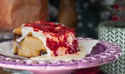 cinnamon roll caindo muita cobertura de leite condensado e geléia de frutas vermelhas e morango