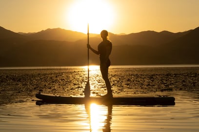 a person standing on sup board at sunset