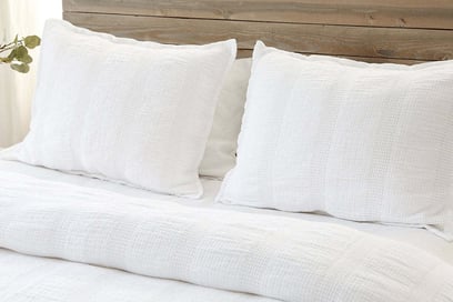 a bed with white linens quilt and pillows on top of a wooden headboard