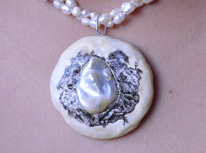 A string of pearls with a pendant made of clay. Pendant includes a  hand-drawn landscape in ink.