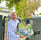 A man in a white shirt stands at his front gate holding a painting of pigs