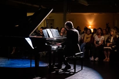 A backlit pianist plays on a grand piano while the audience listens in the background