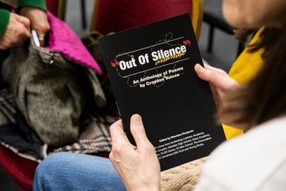 a person holding a book with black cover and white text decorated with colourful doodles