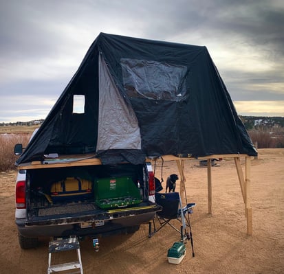 A truck with a cookstove on it's tailgate, cargo in it's bed, and a fold-out tent on it's bed