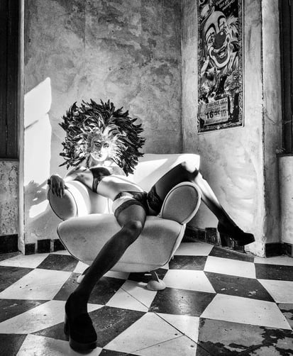 Belle jeune femme en sous vetements et bas noirs portant un masque vénitien dans un fauteuil 