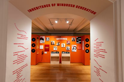 an orange exhibition display of portraits and text, bordered by a white wall with orange text