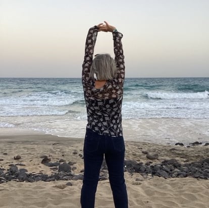 a woman standing on a beach with her arms up in the air