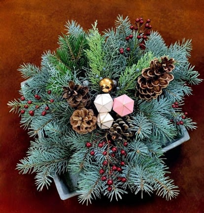 Aranjament de iarnă cu crengi de brad, conuri, bobițe roșii și decorațiuni festive într-un vas.