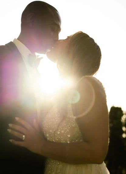Golden hour kiss between bride and groom with sunlight streaming through