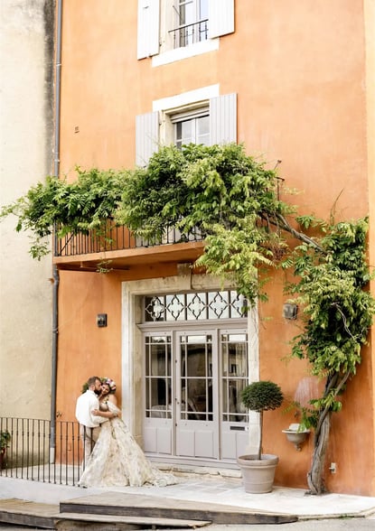 Wide shot of couple in front of ochre building with climbing vine — kiss on the cheek, fine art