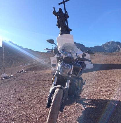 a motorcycle parked in a desert area with a statue of jesus on the side of Cristo Redentor Andes