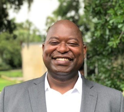 Dollar Harmony Coach Wildo in a suit and white shirt smiling