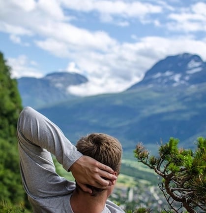 Homme allongé en montagne main gauche derrière la tête regardant un haut sommet un peu enneigé