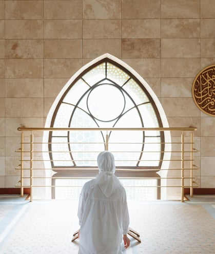 femme portant le hijab de dos devant une fenêtre remplie de lumière annour