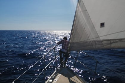 Un hombre sentado en la proa de un velero, con la vela a su espalda, navegando