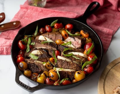 a cast iron skillet with steak steak and tomatoes