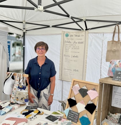 La créatrice derrière son stand sur un marché de créations artisanales