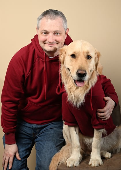 a man in a red hoodie and a golden retriever in a red sweater posing next to each other