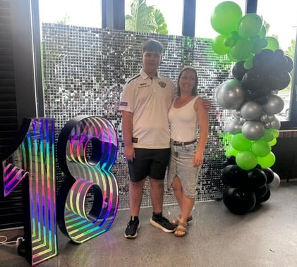 Jayden and mum in front of a silver shimmer backdrop with 18 marquee number at his birthday at the Distillery Beenleigh.