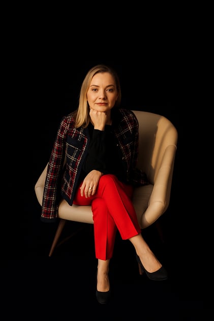 Imagem da Dra. Maiara Conzatti sentada em um poltrona bege. Fundo da imagem preto.
