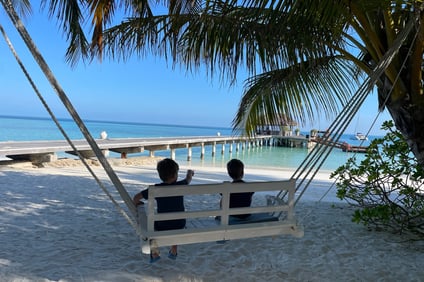 two people sitting on a swing chair in the sand