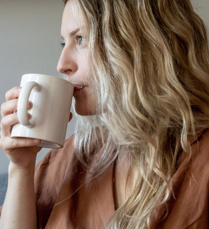 a woman with blonde hair and a brown shirt is drinking a cup of coffee