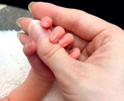 Newborn baby holding mothers thumb for the first time, symbolizing early motherhood bond and emotional connection
