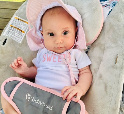 A newborn baby girl with a pink sunhat sitting in a bouncer, looking at the camera