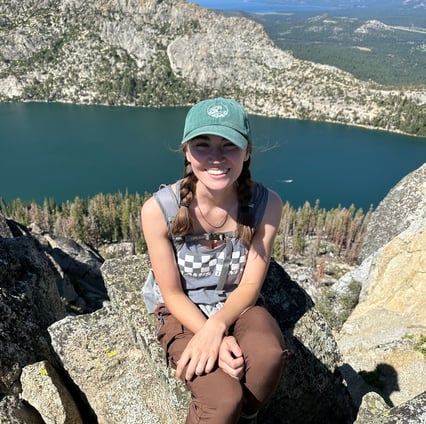 the author sitting on a rock in the mountains. in the background is a lake and a forest of pine.