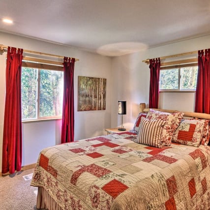 Bright guest bedroom with forest views, red curtains, and queen memory foam bed.