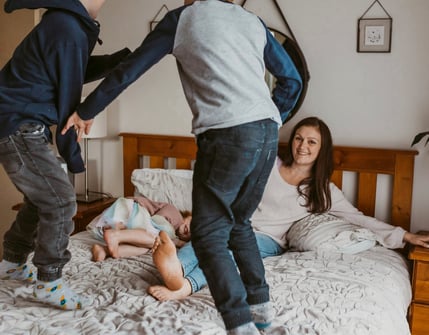 two young boys jumping on a bed with their mother