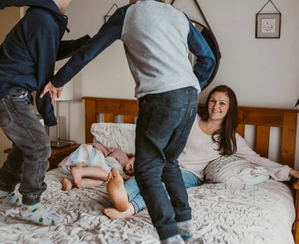 two young boys jumping on a bed with their mother