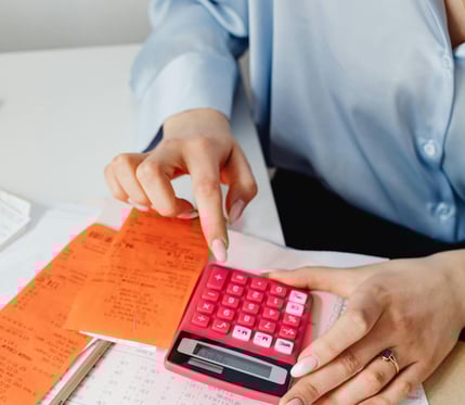 Person using a pink calculator while organizing receipts and documents on a desk.