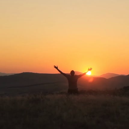 a person standing on a hill with their arms up in the air