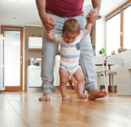 a man holding a baby's hand while standing on a hardwood floor