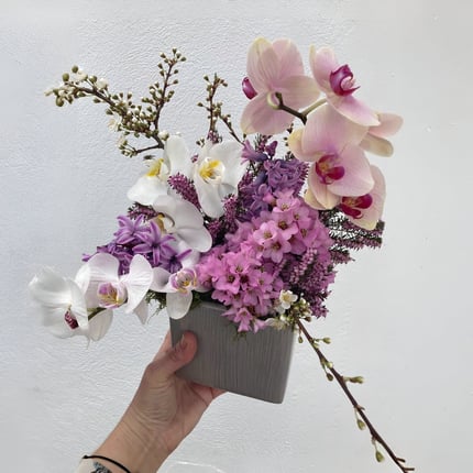 Aranjament floral în nuanțe de roz, mov și alb, cu orhidee și flori de primăvară, într-un ghiveci.