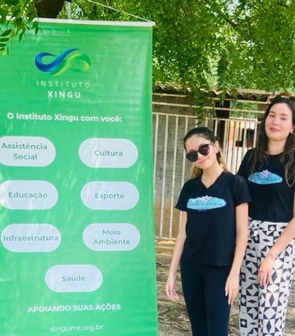 Uma criança e uma mulher em pé ao lado de um banner do Instituto Xingu MT